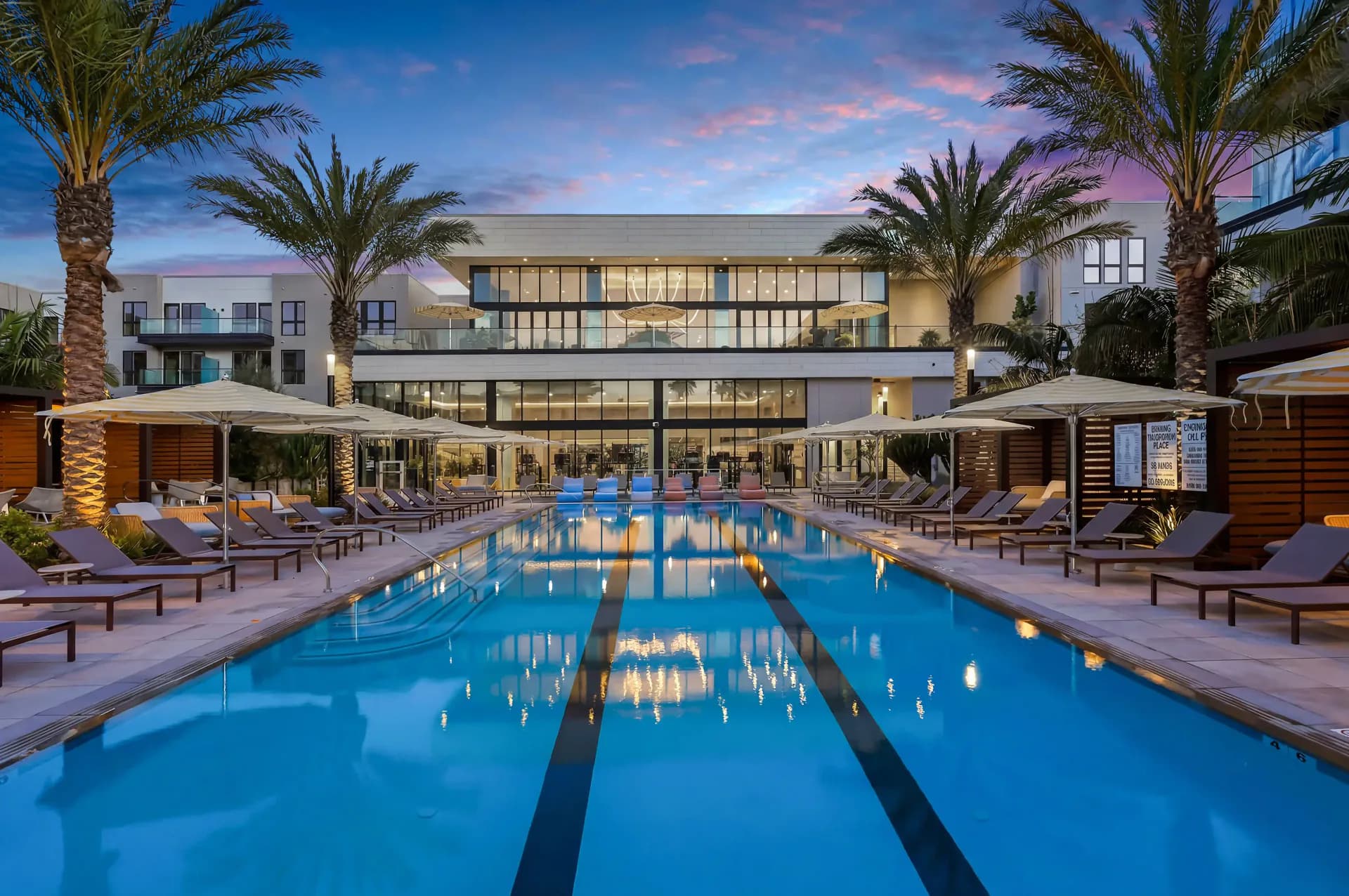 Symmetrical twilight photograph of a swimming pool framed by palm trees and a residential clubhouse