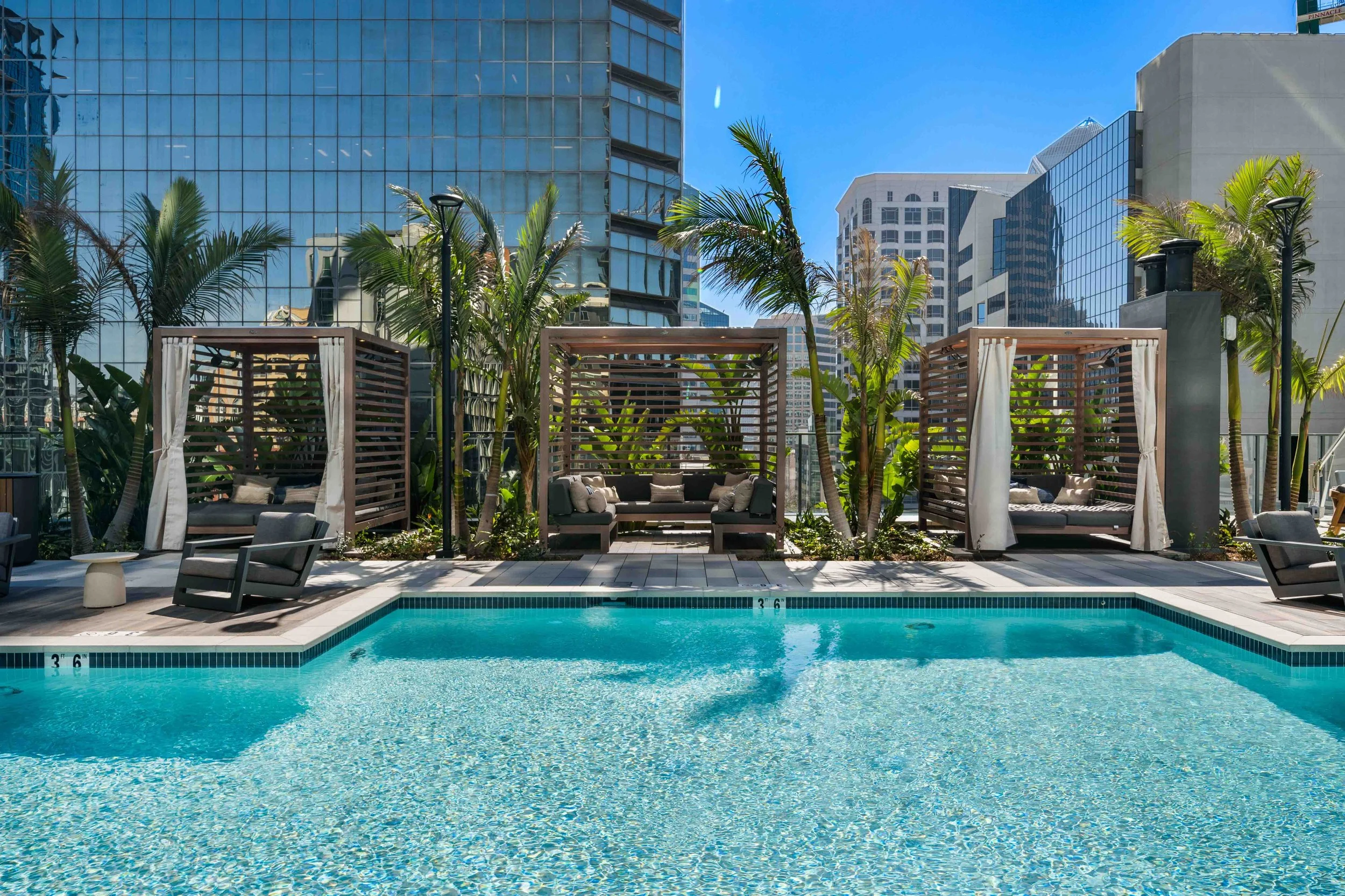 Swimming pool and furnished cabanas at The Lindley, surrounded by city buildings.