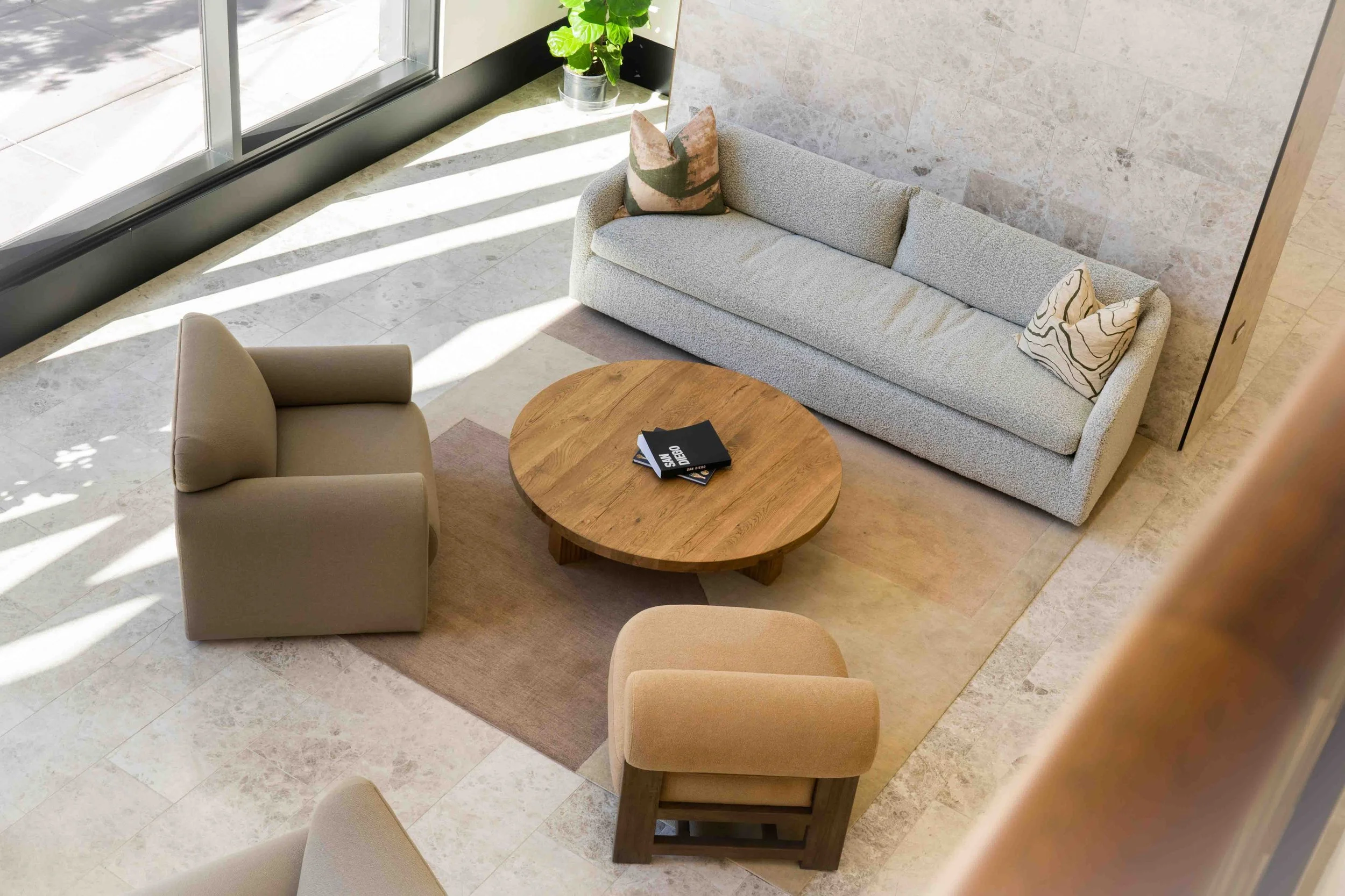 Curved sofa and lounge chairs around a round table beside windows at The Lindley.