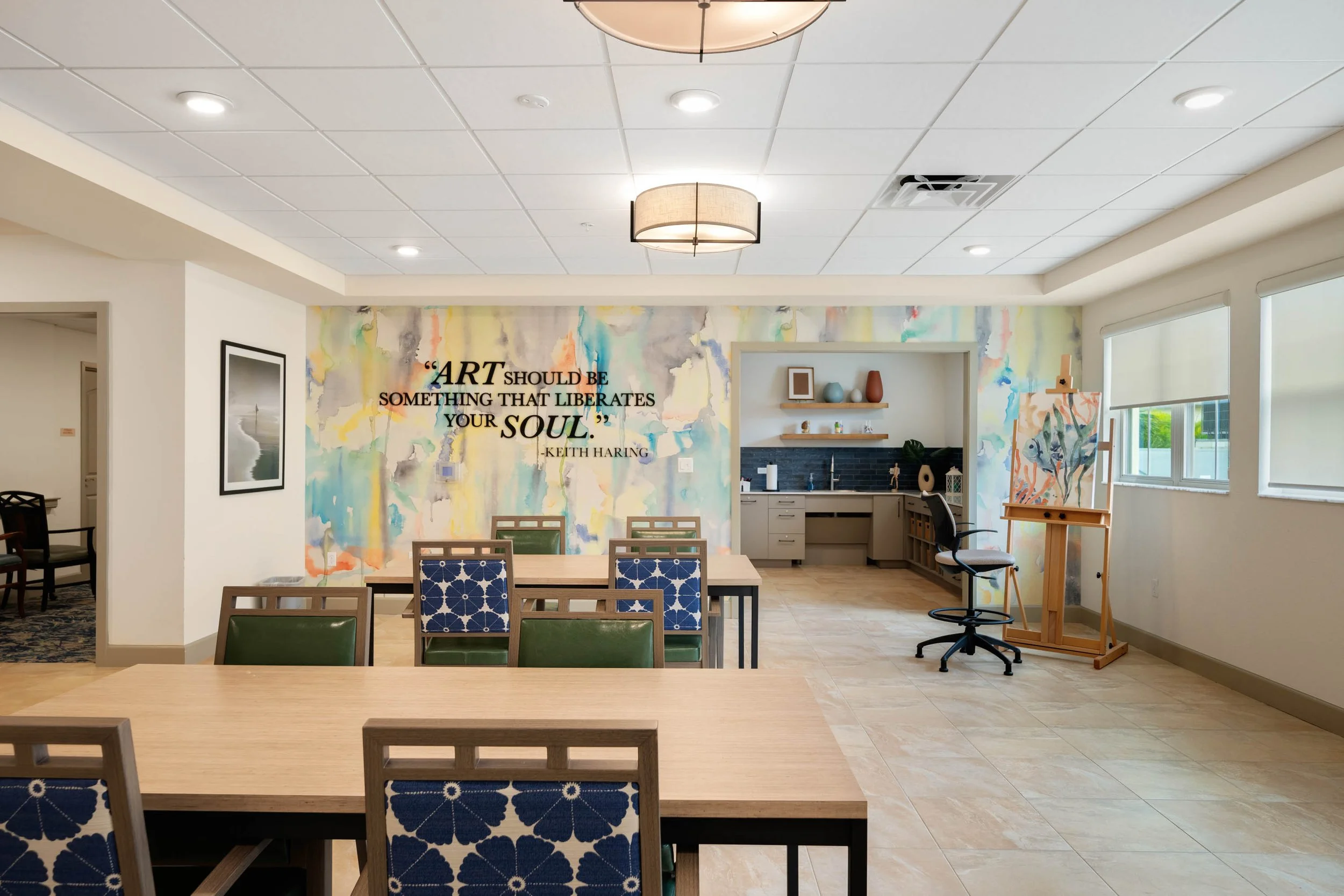 Activity room at The Glades at ChampionsGate with tables, chairs, and a colorful art mural.