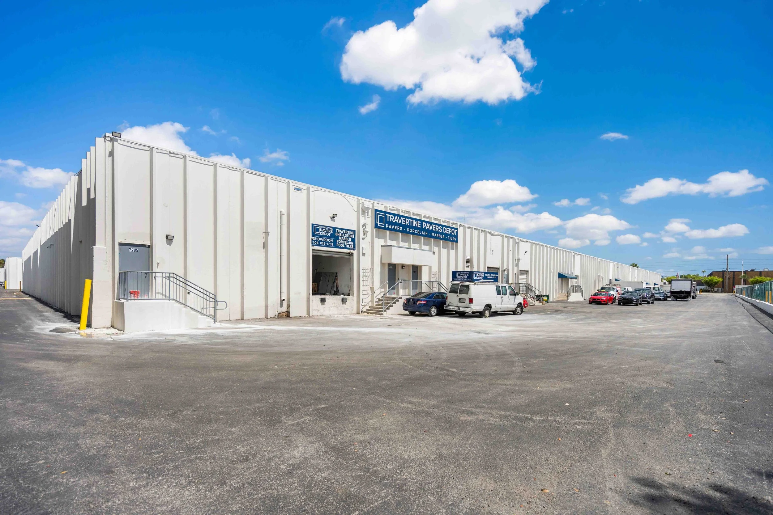 Long white industrial building at Airport Trade Center with entrances and parked vehicles.