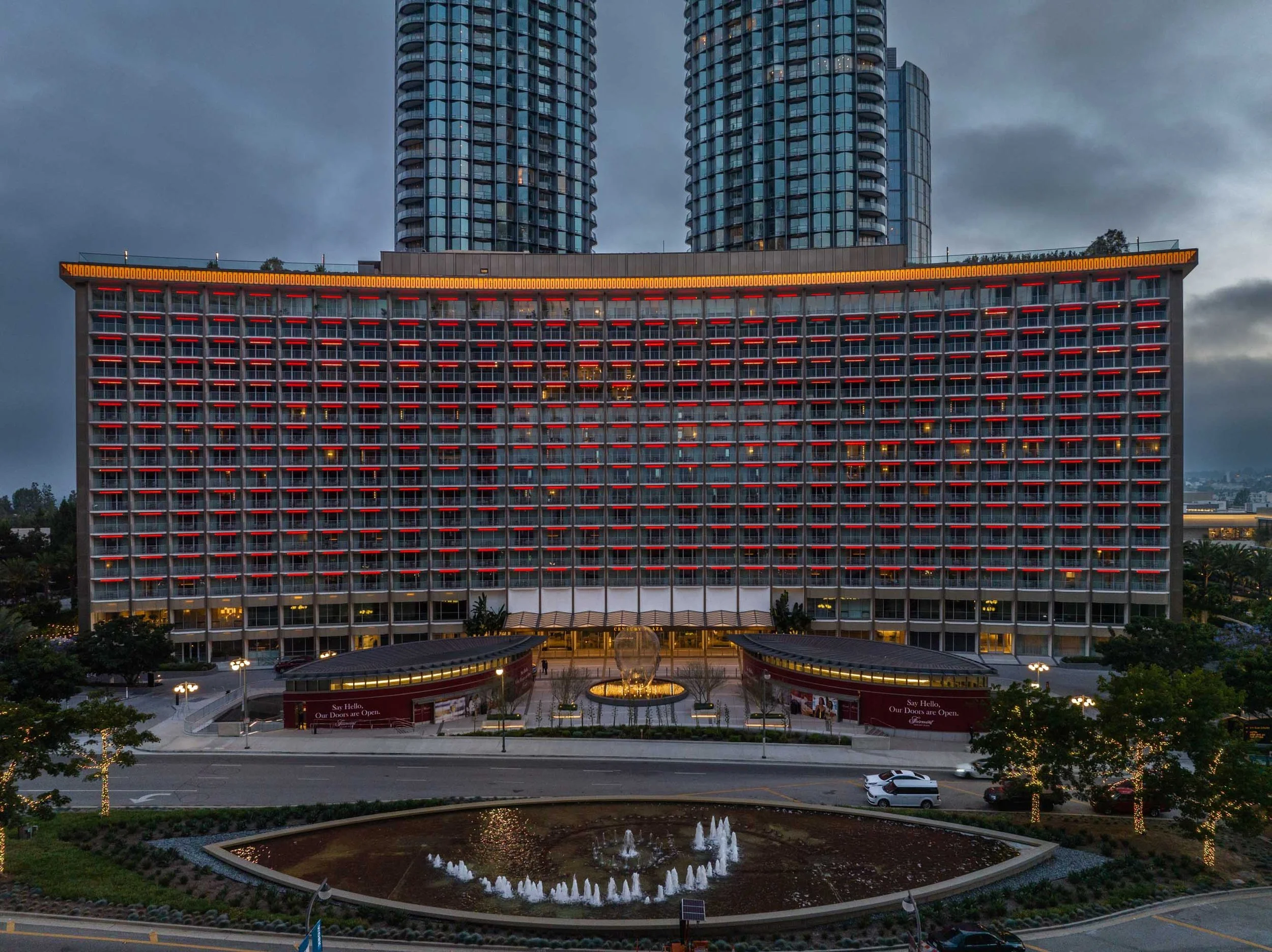Fairmont Century Plaza facade at dusk with red balcony lighting and towers behind it.