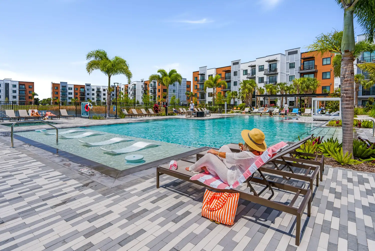 Outdoor apartment pool with furnished deck and a resident relaxing on a lounge chair