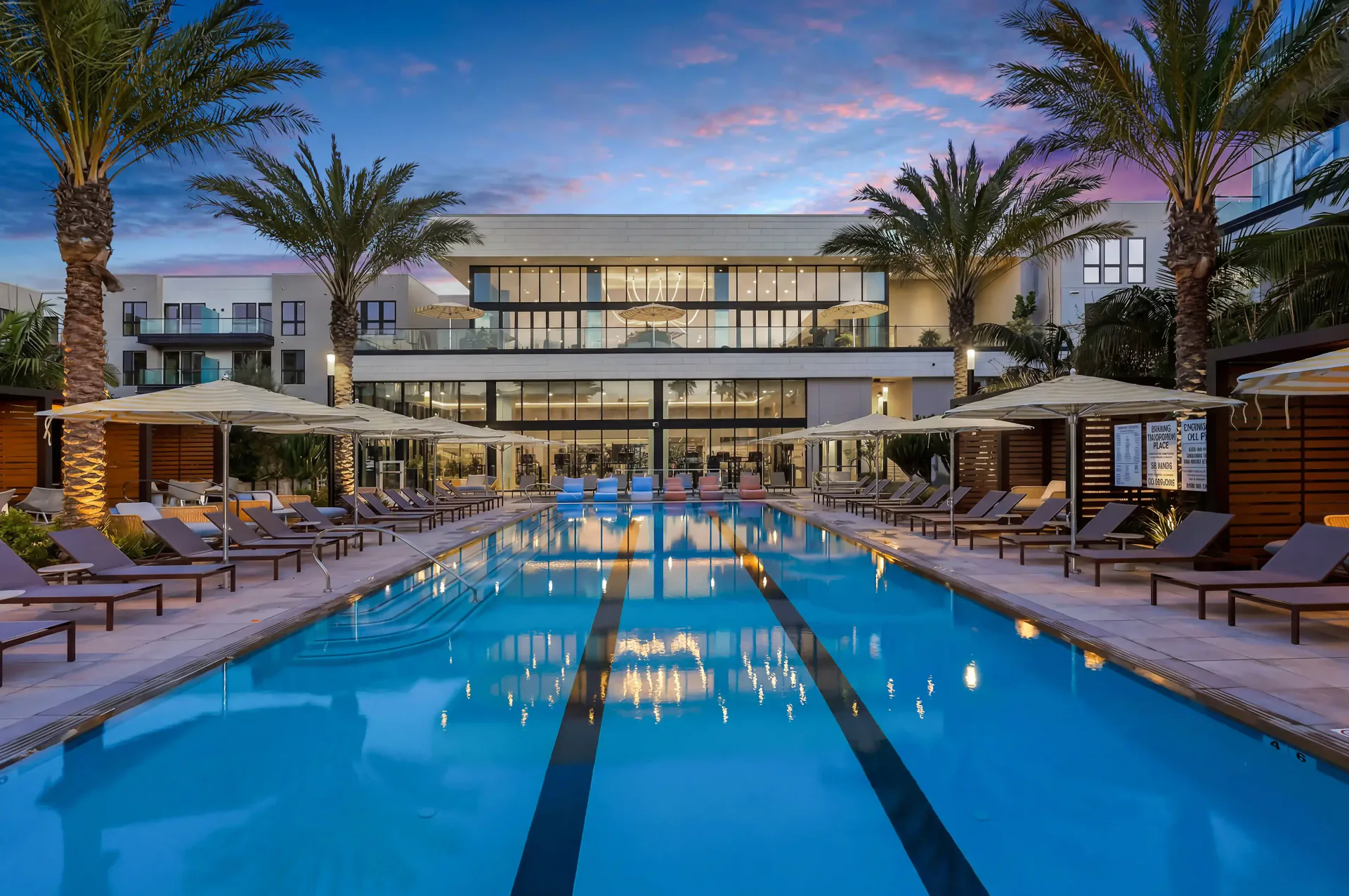 Symmetrical twilight photograph of a swimming pool framed by palm trees and a residential clubhouse