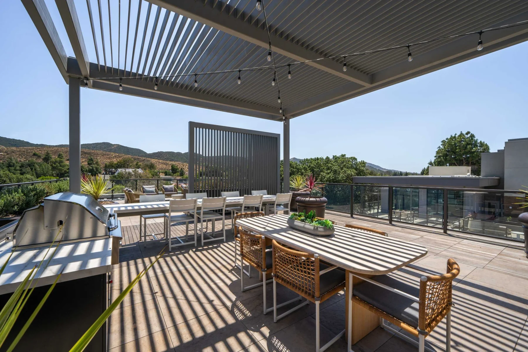 Outdoor rooftop terrace with dining tables, pergola and distant hills
